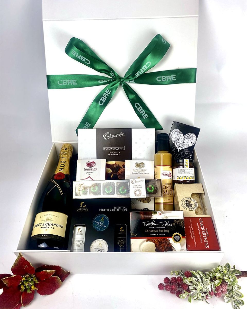 White gift box finished with a client-branded green ribbon, filled with Champagne and gourmet treats